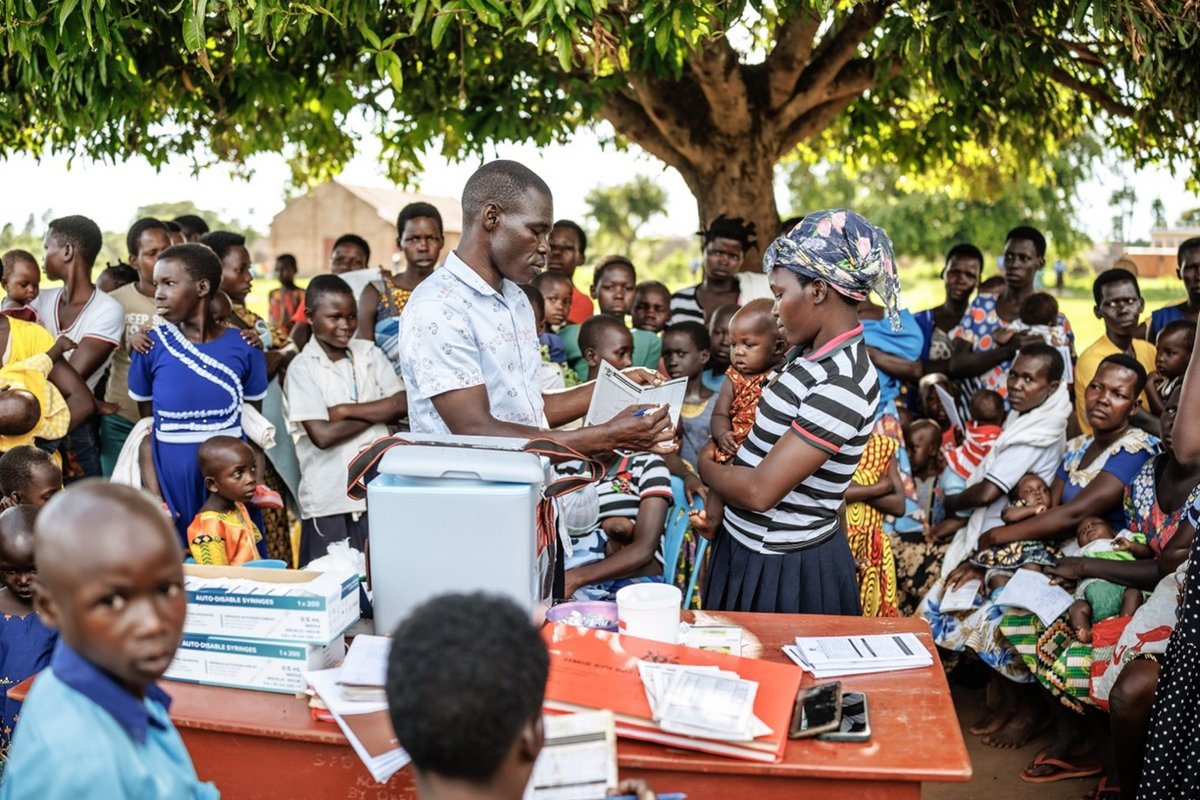 2025, Distrikt Apac, Uganda. Im Rahmen eines Community-Outreachs erklärt ein Gesundheitshelfer einer Mutter, dass der R21/Matrix-M-Malariaimpfstoff in vier Dosen verabreicht wird – im Alter von 6, 7, 8 und 18 Monaten. Mit Unterstützung von WHO, Gavi, UNICEF und weiteren Partnern ist Uganda das 19. afrikanische Land, das den Malariaimpfstoff in sein reguläres Impfprogramm aufgenommen hat. Der offizielle Start im Distrikt Apac im Norden Ugandas markierte den bislang größten Rollout und richtet sich an über 105 Bezirke mit hoher und mittlerer Übertragungsrate.